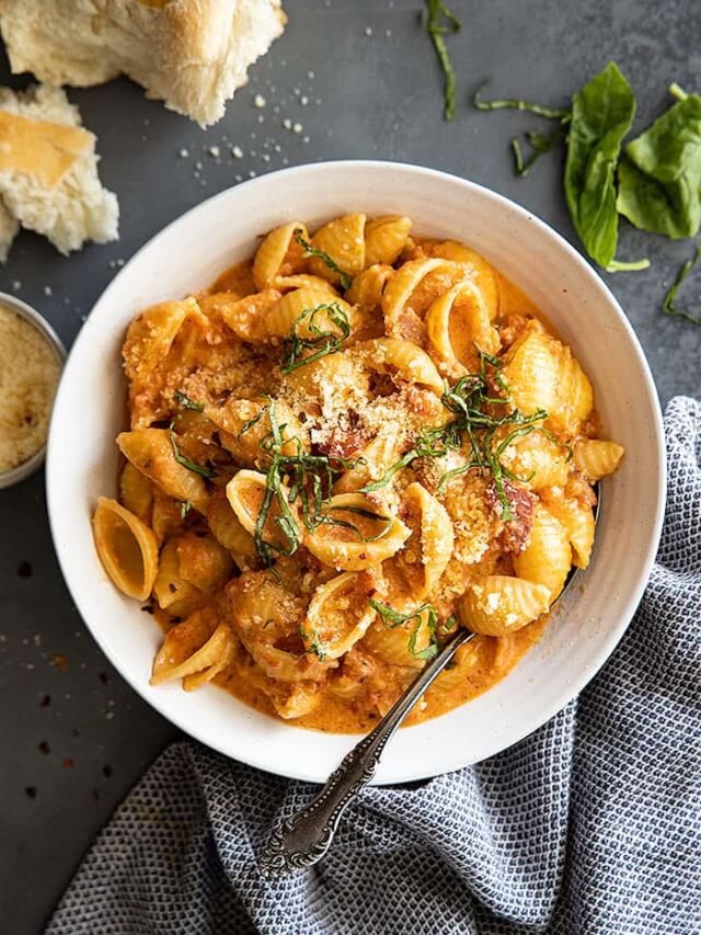 Overhead view of pasta with sauce in a white bowl. Garnished with fresh basil and parmesan cheese.