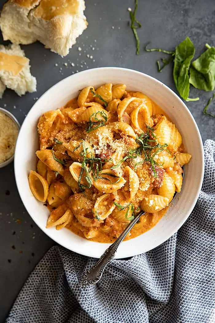 Overhead view of pasta with sauce in a white bowl. Garnished with fresh basil and parmesan cheese. 