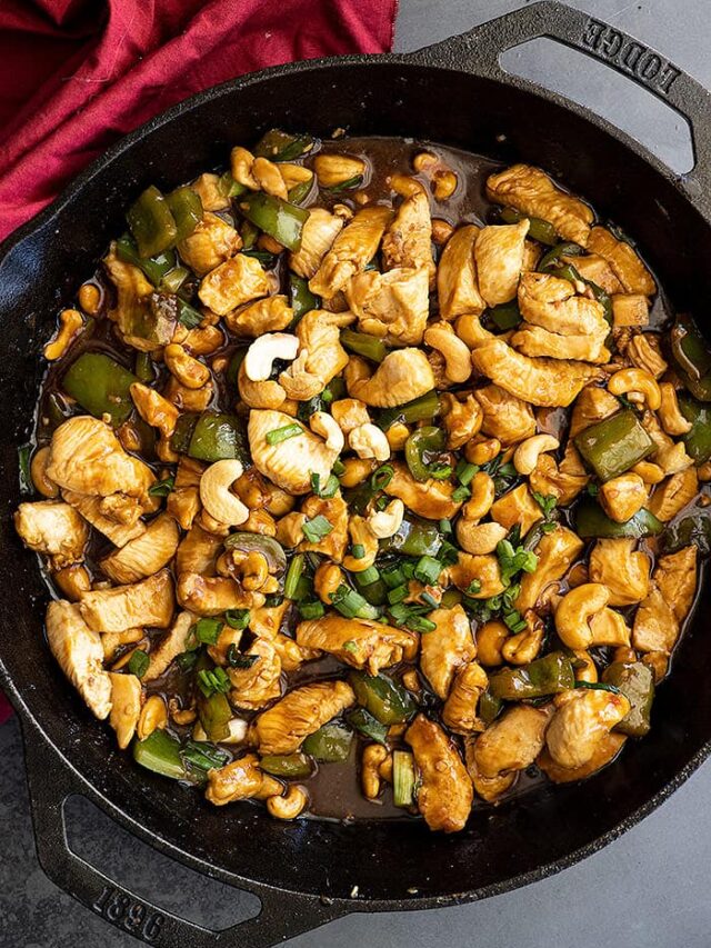Overhead view of cashew chicken in a cast iron skillet garnished with green onions. Red napkin off to the side.