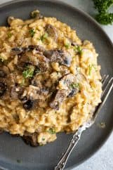 Risotto piled high on a dark plate. Garnished with parmesan and parsley.