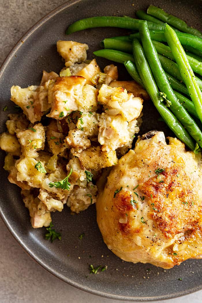 A serving of the stuffing and chicken on a plate with fresh green beans on the side. 