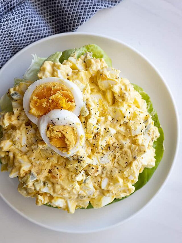 Overhead view of a large bowl of egg salad. Topped with 2 slices of hard boiled egg and fresh ground pepper.