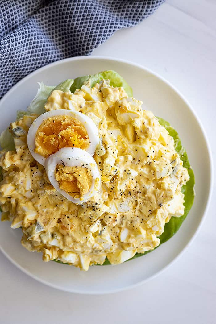 Overhead view of a large bowl of egg salad. Topped with 2 slices of hard boiled egg and fresh ground pepper. 