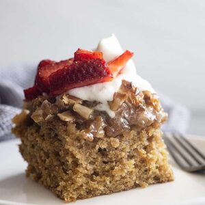 A large piece of Oatmeal Cake on a white plate topped with whipped cream and strawberries.
