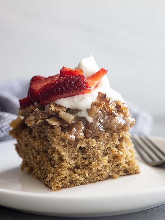 A large piece of Oatmeal Cake on a white plate topped with whipped cream and strawberries.