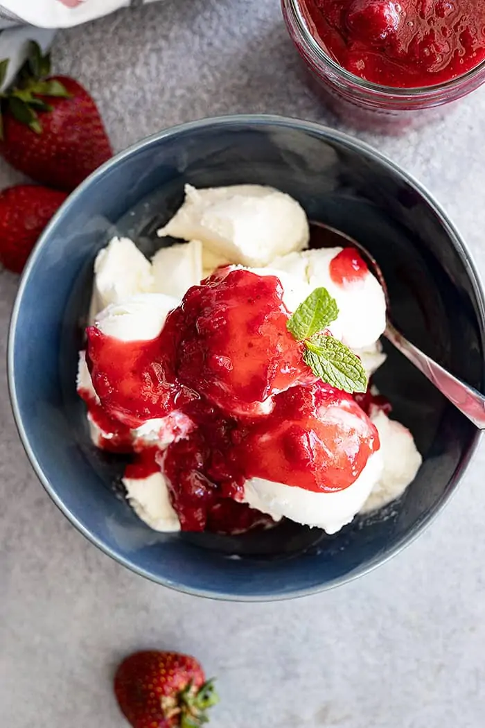 Overhead view of sauce spooned over vanilla ice cream in a blue bowl garnished with mint.