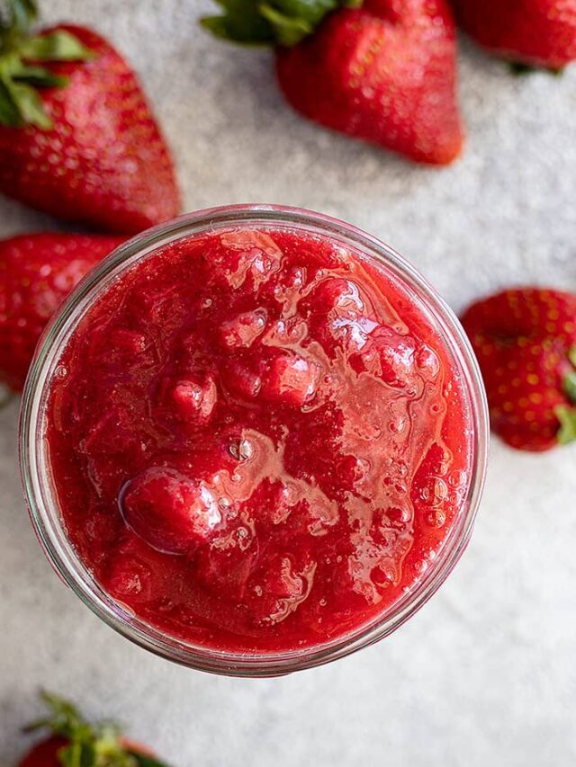 Overhead view of sauce in a jar. Fresh strawberries scattered around for embellishment.