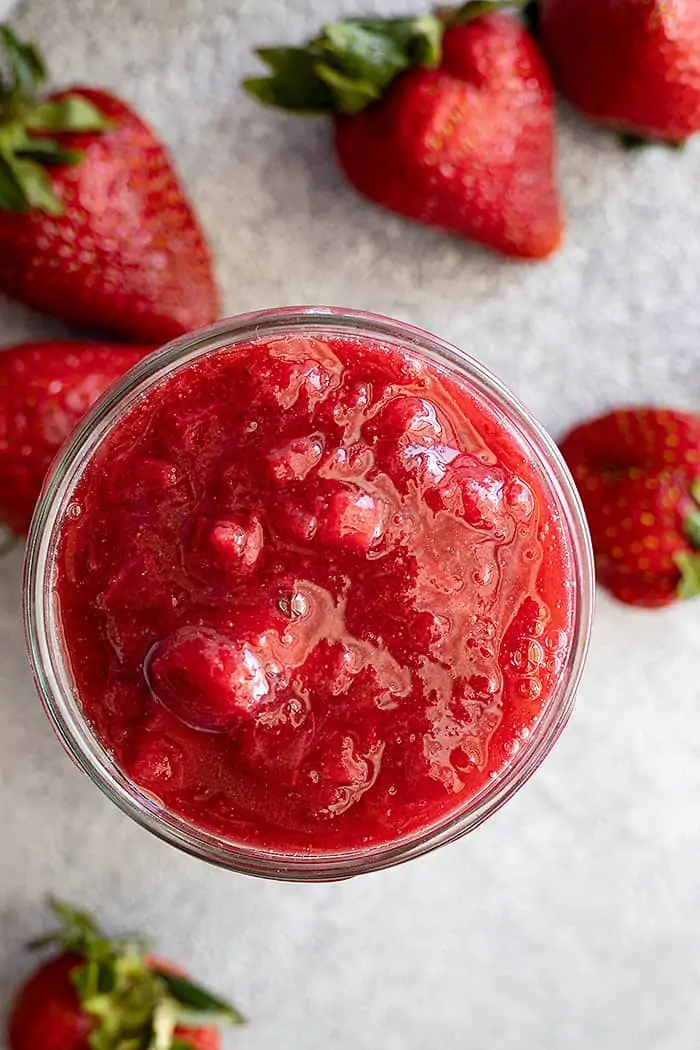 Overhead view of sauce in a jar. Fresh strawberries scattered around for embellishment.