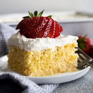 A piece of tres leches cake on a small plate topped with a fanned out strawberry.