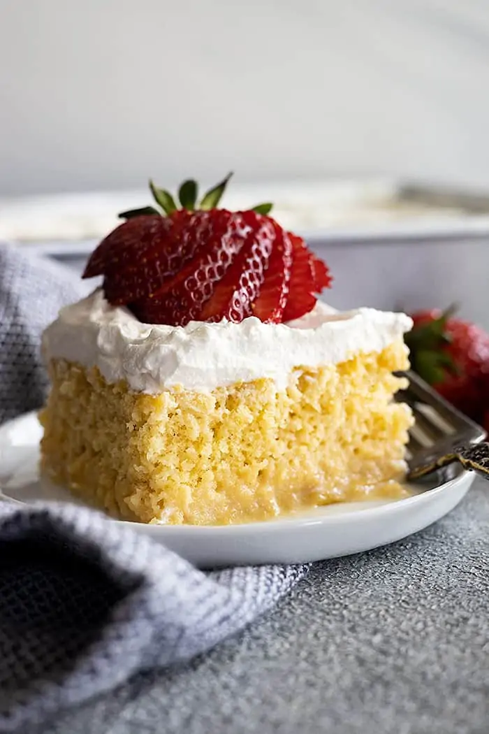 A piece of tres leches cake on a small plate topped with a fanned out strawberry. 