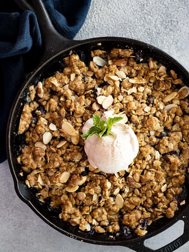 Overhead view of blueberry crisp fresh from the oven. Topped with a big scoop of ice cream and a piece of fresh mint.