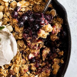 Close up of blueberry crisp with a spoon in it. Topped with a scoop of ice cream.