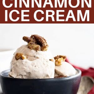 Two scoops of cinnamon ice cream in a small black bowl topped with pecans.