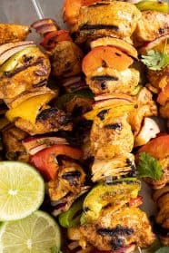 Close up picture of grilled chicken kebabs. Garnished with lime slices and cilantro.