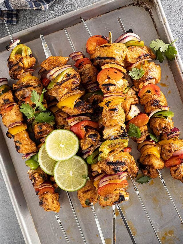 A pan filled with chicken kebobs fresh off the grill. Garnished with fresh lime slices and cilantro.