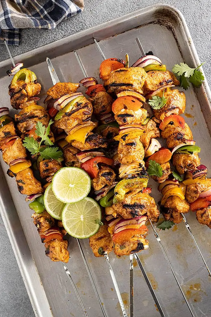 A pan filled with chicken kebobs fresh off the grill. Garnished with fresh lime slices and cilantro. 