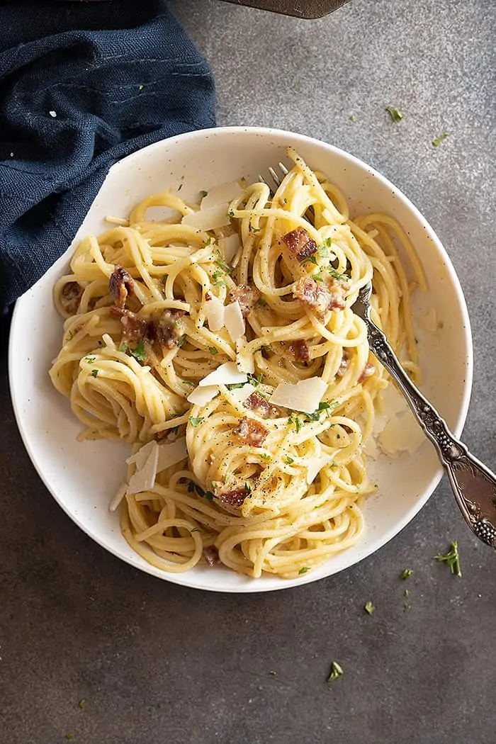 Overhead view of pasta swirled in a white dish and a navy napkin off to the side. Topped with shaved parmesan and parsley. 