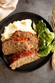 Overhead view of slices of tender meatloaf over mashed potatoes with a spinach salad.