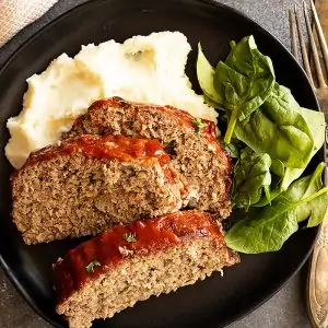 Overhead view of slices of tender meatloaf over mashed potatoes with a spinach salad.