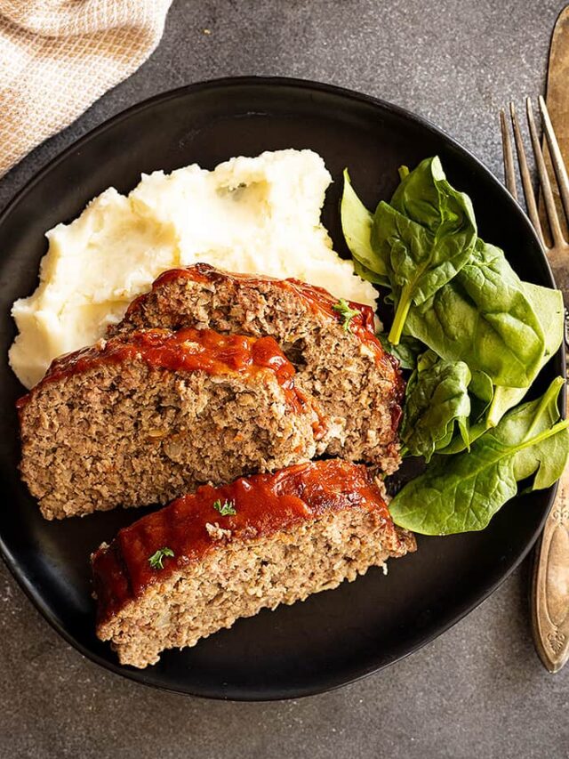Overhead view of slices of tender meatloaf over mashed potatoes with a spinach salad.