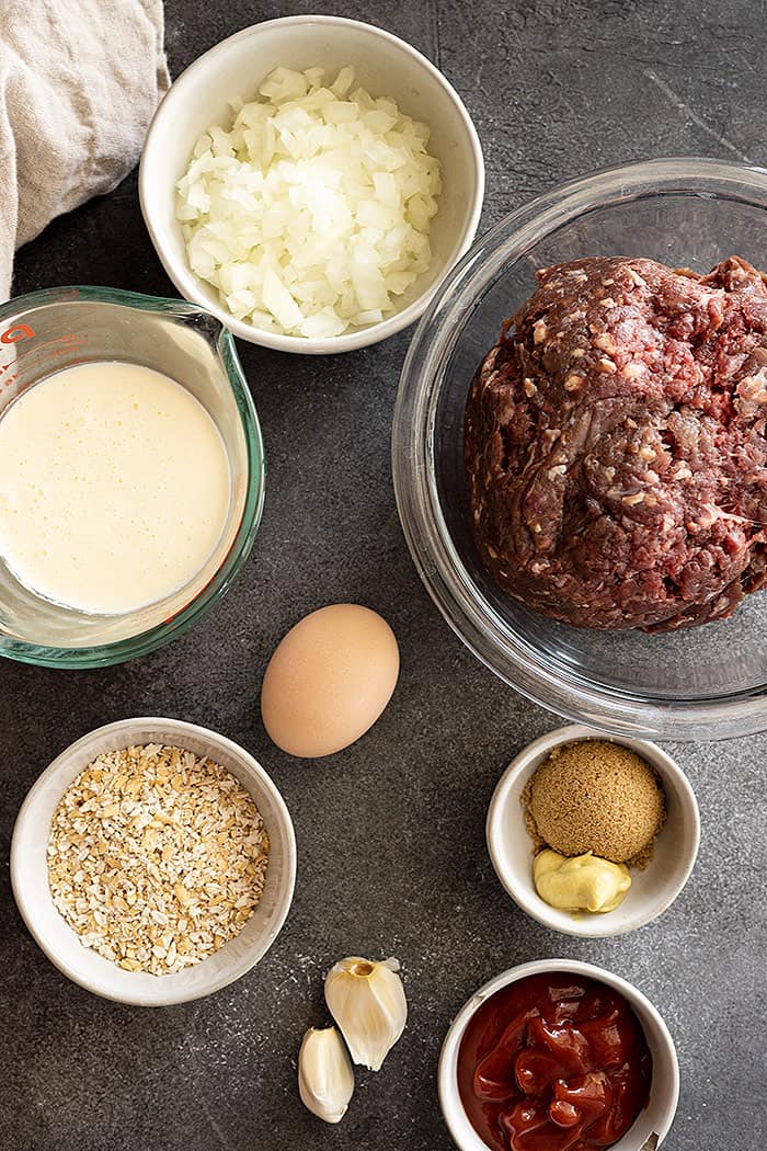 Ingredients needed to make Old Fashioned Meatloaf: ground beef, onion, garlic, egg, oats, milk, brown sugar, ketchup, and mustard. 