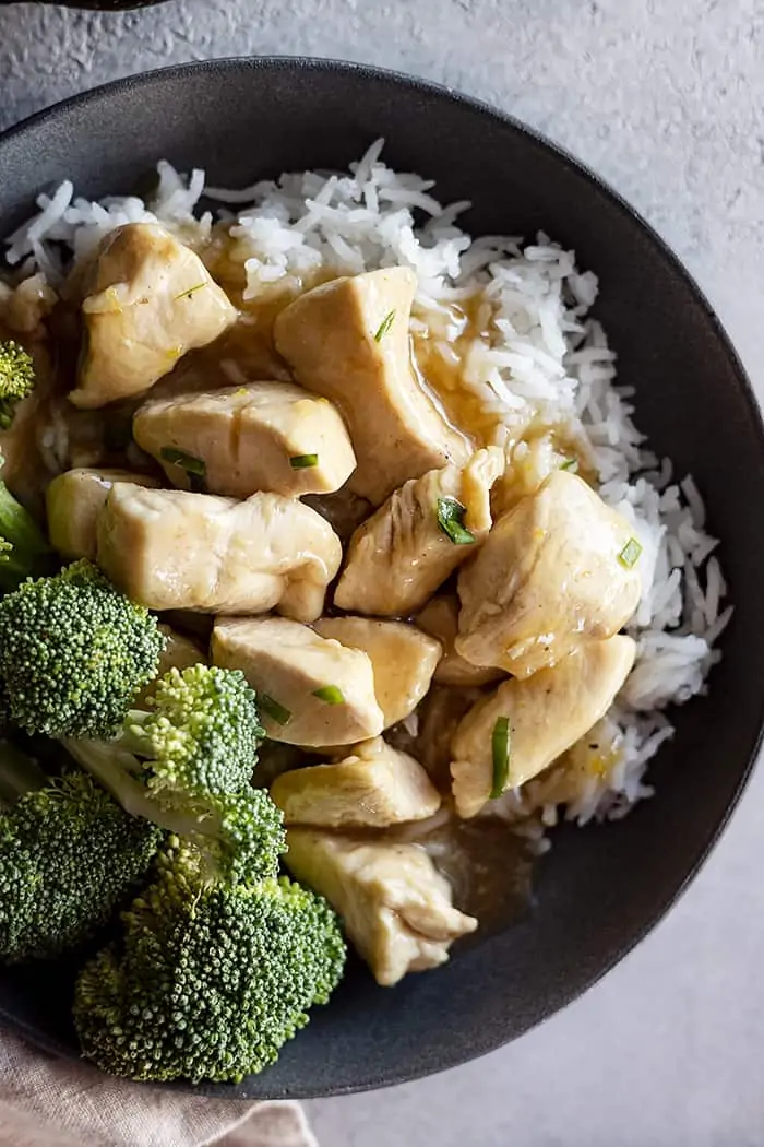 Overhead view of chinese lemon chicken in a bowl over white rice and a side of steamed broccoli. 