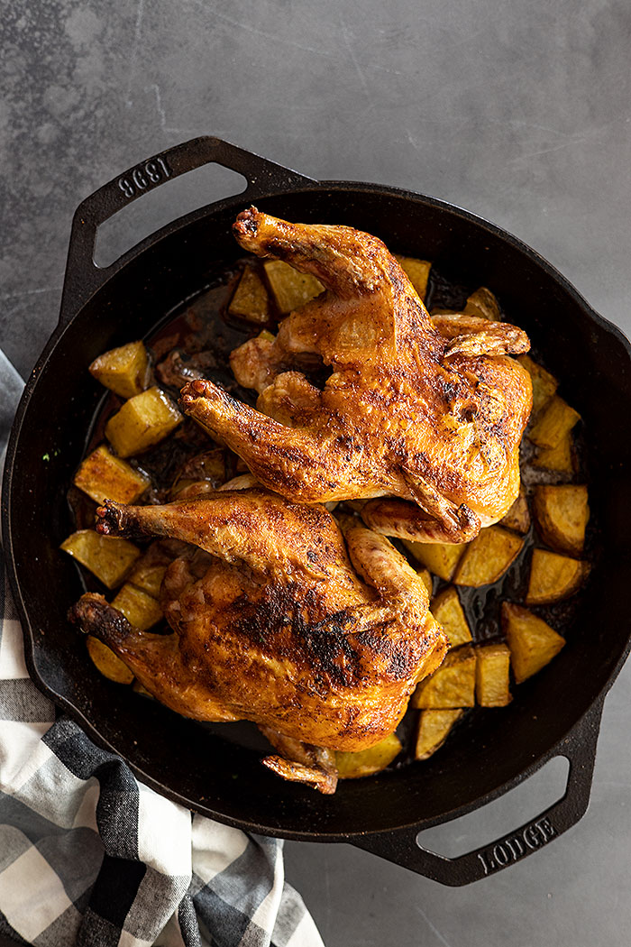 Overhead view of roasted cornish hens over potatoes in a cast iron skillet.
