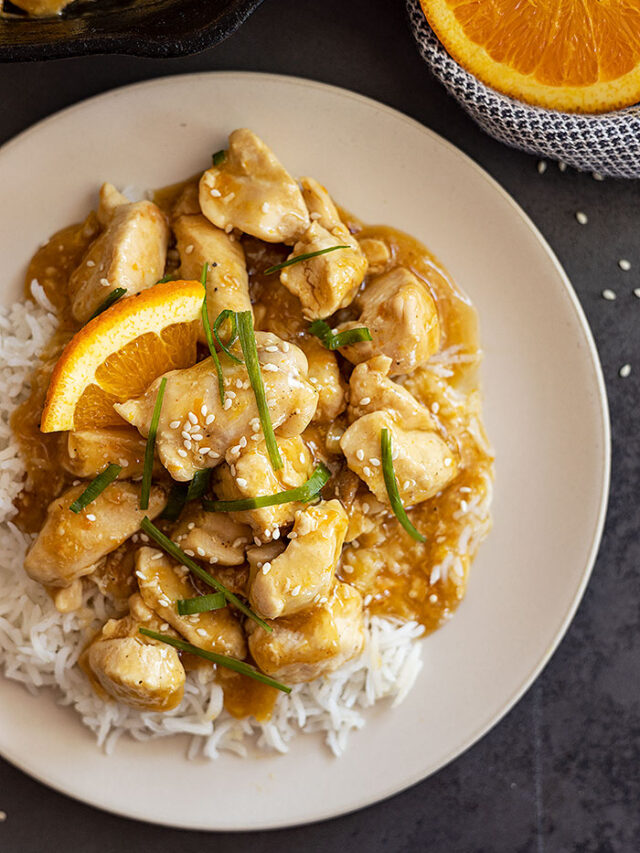 Overhead view of easy orange chicken on a bed of rice and garnished with green onions, sesame seeds, and orange slices.