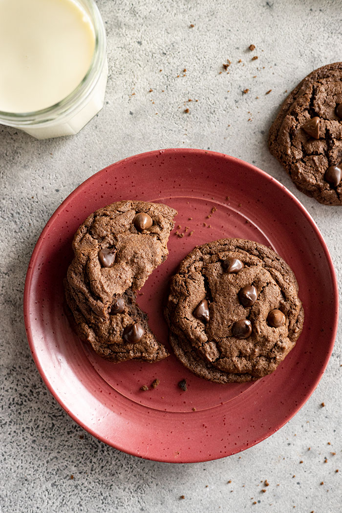 Cookies on a red plate with visible crumbs around and a glass of ice cold milk. 