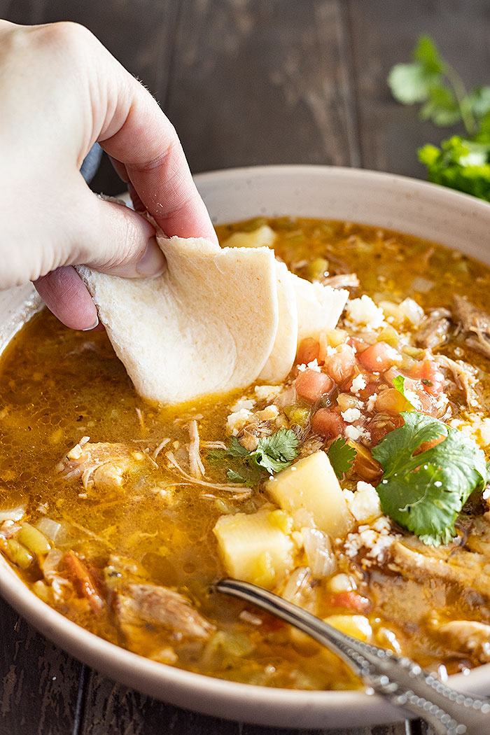 Hand holding a folded tortilla dipping it into the green chile stew.
