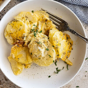 Overhead view of garlic herb potatoes au gratin on a plate, garnished with fresh parsley and black pepper.