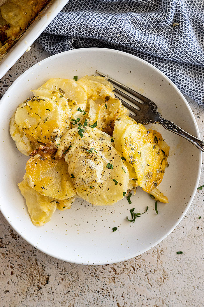 Overhead view of garlic herb potatoes au gratin on a plate, garnished with fresh parsley and black pepper.