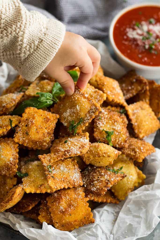 hand holding a piece of toasted ravioli