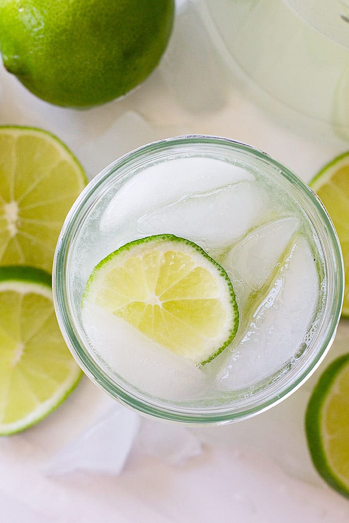 Top down view of a fresh limeade recipe in a glass with a slice of lime and ice. 