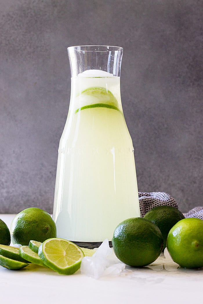A tall pitcher of homemade limeade with fresh limes as garnish. 
