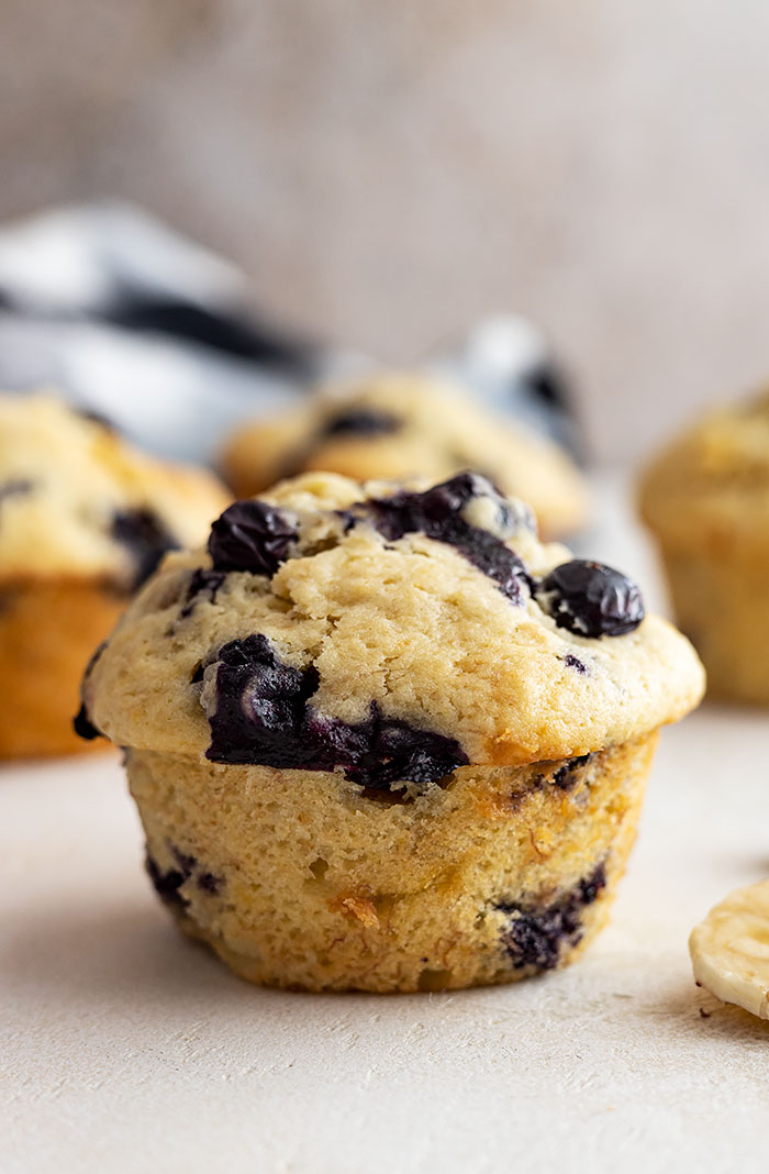 Close up of 1 blueberry muffin with several muffins in the background.