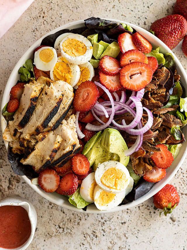 Overhead view of a large bowl of strawberry cobb salad with dressing off to the side.