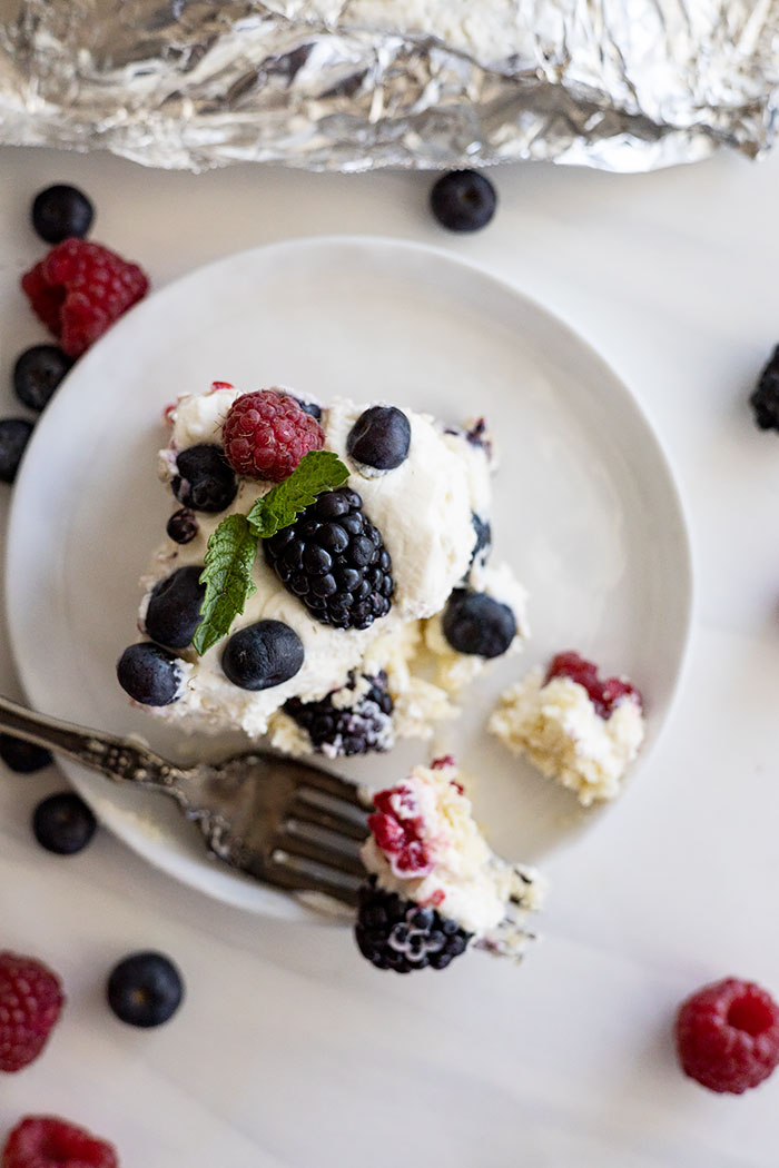 Overhead view of a piece of cake on a white plate with berries scattered around.