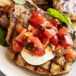 Close up of pork chop topped with melted mozzarella and bruschetta.