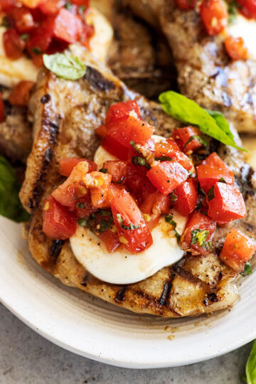 Close up of pork chop topped with melted mozzarella and bruschetta.
