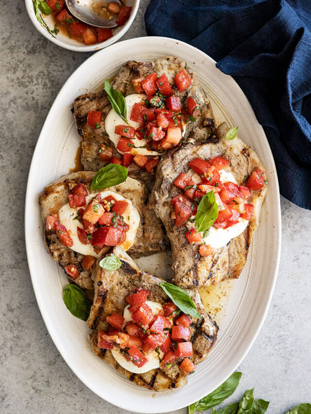 Overhead view of bruschetta pork chops on a serving platter garnished with fresh basil.