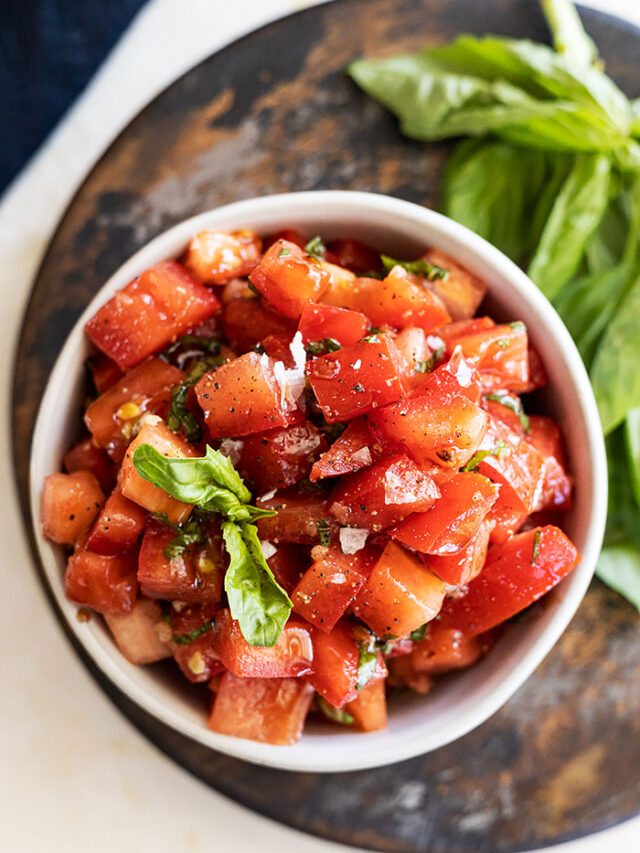 Overhead view of bruschetta in a bowl garnished with a basil leaf and flakey sea salt.