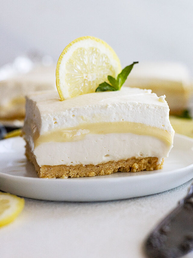 A piece of lemon dessert on a plate garnished with a lemon slice and mint.