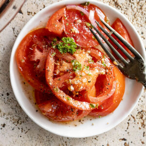 Marinated tomatoes on a white plate with a fork off to the side.