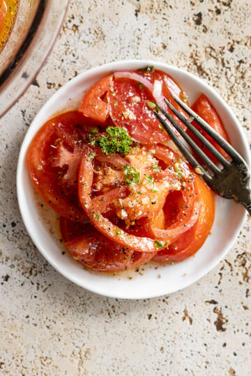 Marinated tomatoes on a white plate with a fork off to the side.