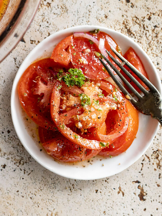 Marinated tomatoes on a white plate with a fork off to the side.