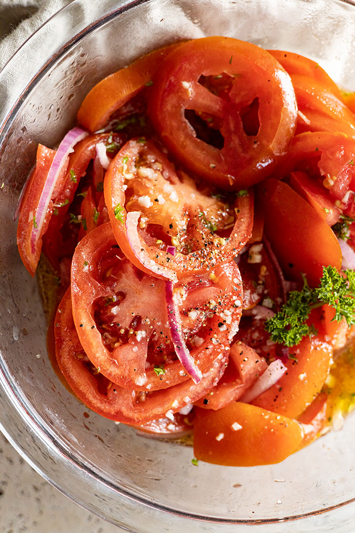 Close up of marinated tomatoes in a bowl. Garnished with cracked pepper and flakey salt. 