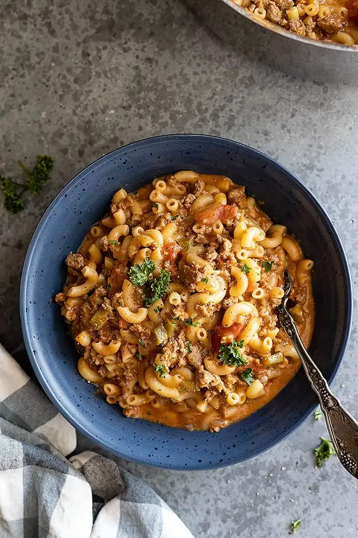 Overhead view of goulash in a blue bowl garnished with parsley.