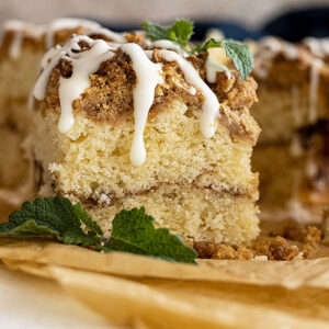 Slice of coffee cake with icing drizzled on top. Mint in the corner for garnish.