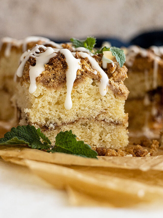 Slice of coffee cake with icing drizzled on top. Mint in the corner for garnish.